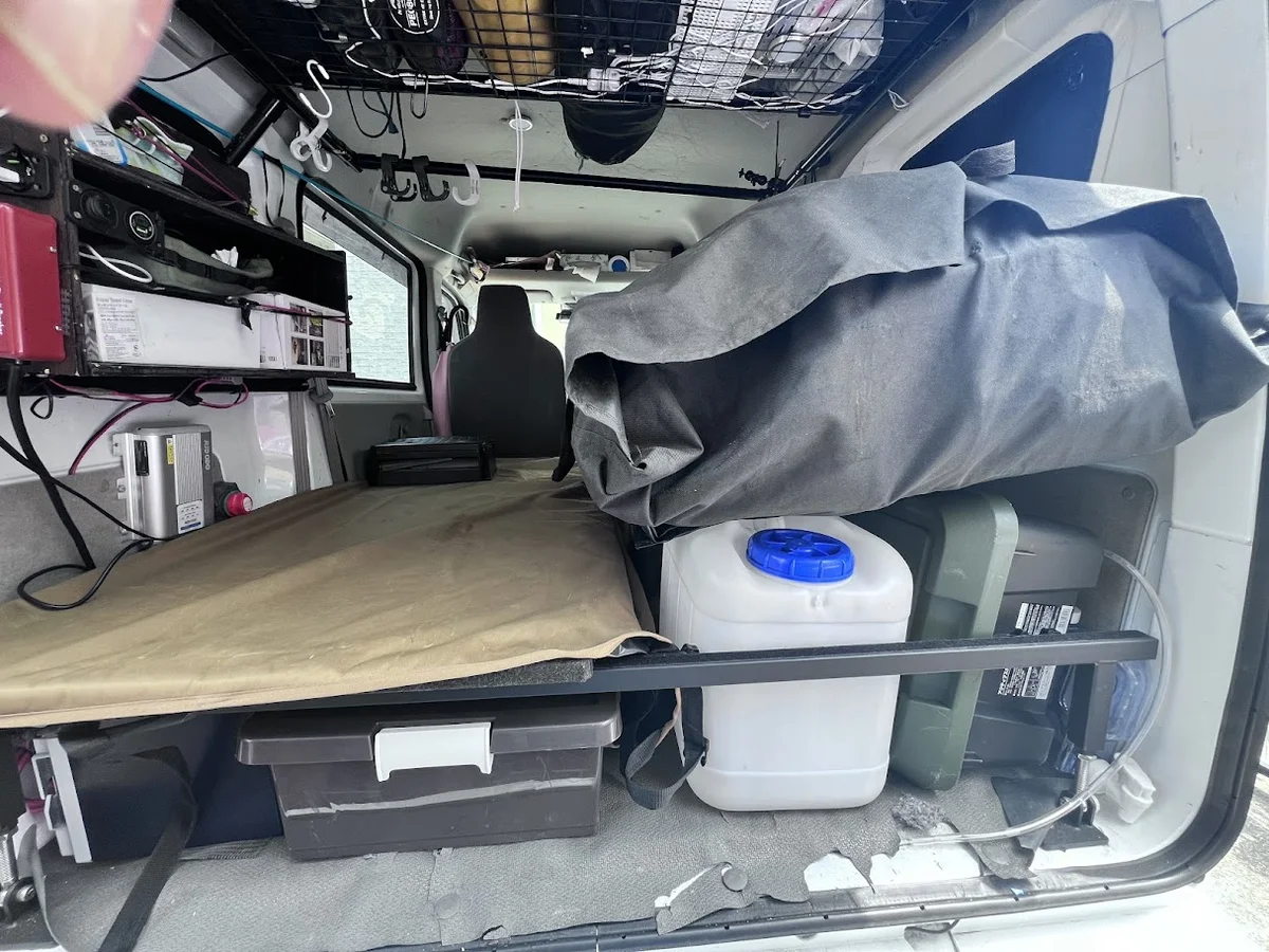 軽バンの荷室に半分ベッドを残し、右側にポリタンク、RVボックス、畳んだゴムボートを積んだ釣り車中泊レイアウト