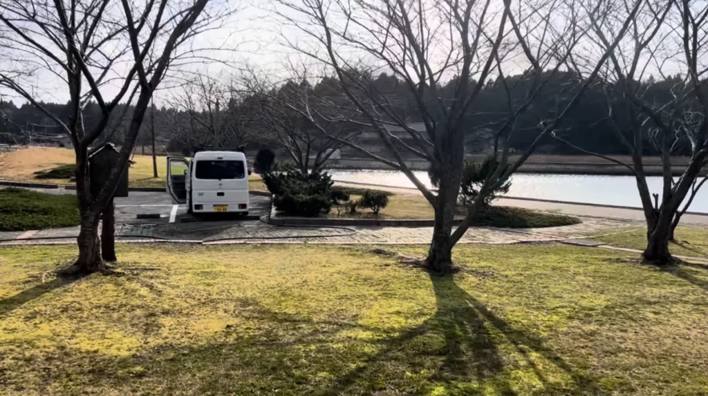 湖の近くのRVパークに白い軽バンを停めている様子。電源付き駐車スペースで車中泊しやすい環境を示している。